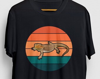 Op de afbeelding: Zwart T-shirt met een retro zonsondergang-grafiek met een baardagame hagedis. De grafiek heeft oranje, gele en blauwe strepen.