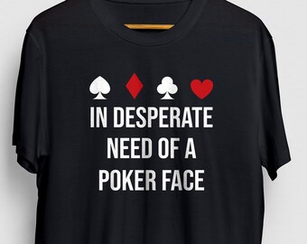 May include: Black t-shirt with white text that reads "IN DESPERATE NEED OF A POKER FACE". Four playing card suits are displayed above the text: a spade, a diamond, a club, and a heart.