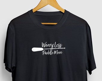 Puede incluir: Camiseta negra con un gráfico blanco que dice "Worry Less Paddle More" con un gráfico de pala blanco.