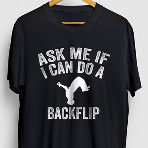May include: Black t-shirt with white text that reads "Ask me if I can do a backflip" and a silhouette of a person doing a backflip.