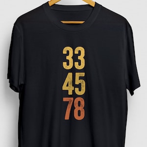Może przedstawiać: Czarny T-shirt z vintage'owym wzorem z numerami 33, 45 i 78 w kolorze żółtym, pomarańczowym i czerwonym.