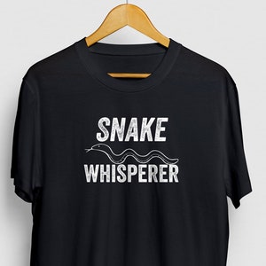 May include: Black t-shirt with a white graphic that says "SNAKE WHISPERER" with a stylized snake image.