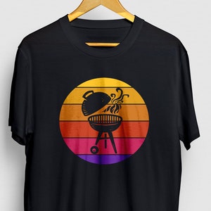 May include: Black t-shirt featuring a retro sunset graphic with a grill and smoke rising from it.