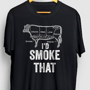 May include: Black t-shirt with a white graphic of a cow cut into different cuts of meat. The text "I'd Smoke That" is below the cow.
