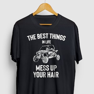 Op de afbeelding: Zwart T-shirt met een witte afbeelding van een terreinwagen en de tekst "The best things in life mess up your hair."