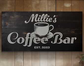 May include: A rectangular black wooden sign with horizontal planks featuring white text that reads Millie's Coffee Bar and EST. 2023. In the centre, there is a white graphic illustration of a coffee cup resting on a matching saucer.