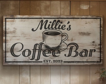May include: A white wooden sign with black text and a black and white illustration of a coffee cup. The sign reads "Millie's Coffee Bar EST. 2023".