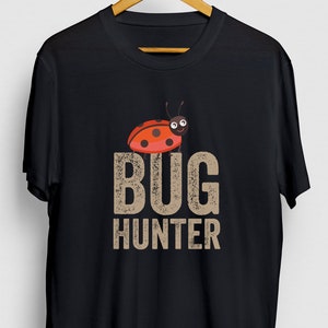 Peut inclure: T-shirt noir avec une coccinelle de dessin animé et le texte "BUG HUNTER" dans une police d'écriture usée.
