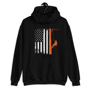 May include: Black hoodie with a distressed American flag design and a silhouette of a person climbing a tree. The tree is orange and the person is climbing with ropes.