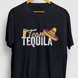 Puede incluir: Camiseta negra con un gráfico blanco que dice "Team Tequila" con un sombrero y un vaso de chupito de tequila.