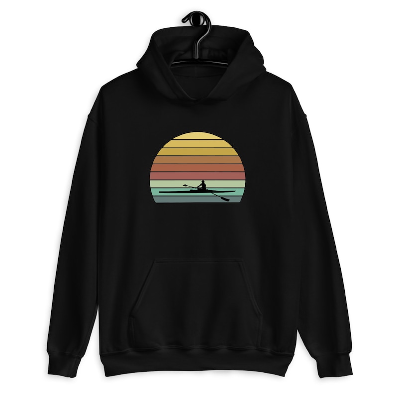Puede incluir: Sudadera con capucha negra con un gr&aacute;fico de puesta de sol retro que presenta la silueta de una persona remando un bote.