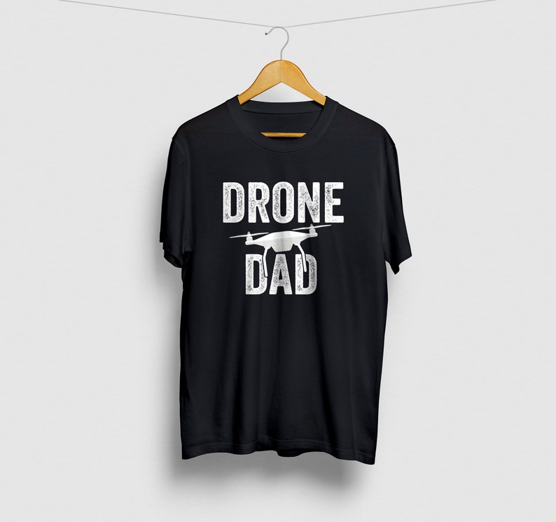 May include: Black t-shirt with white text that reads "Drone Dad" and a white silhouette of a drone.
