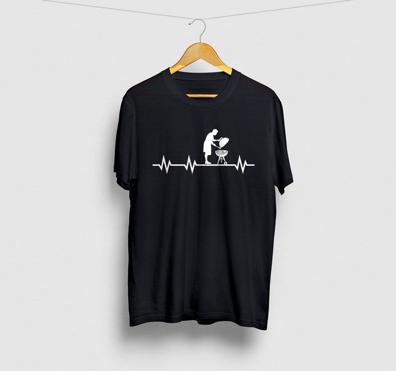 May include: Black t-shirt with a white graphic of a person grilling with a heartbeat line above it.
