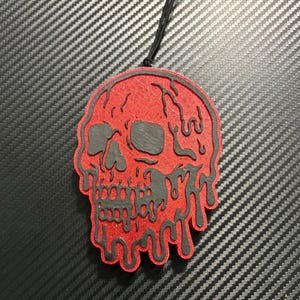 May include: Red skull-shaped air freshener with black dripping details. The air freshener has a black string for hanging. The design is a stylized skull with dripping edges, creating a spooky aesthetic.