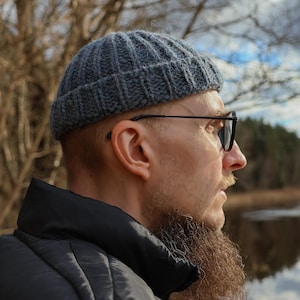 May include: A charcoal grey knit beanie with a ribbed texture and a folded brim. The hat is constructed from a thick yarn, featuring vertical knit lines that run from the crown down to the edge of the cuff, providing a structured fit.