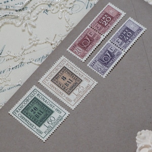 Op de afbeelding: Een verzameling vintage Italiaanse postzegels op een grijze envelop. De postzegels tonen verschillende denominaties en tekst, waaronder "FRANCOBOLLO" en "POSTE ITALIANE". De postzegels zijn in tinten rood, paars en groen.
