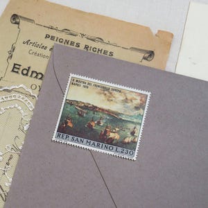 Op de afbeelding: Een vintage postzegel uit San Marino, met een maritieme scène, is bevestigd op een grijze envelop. De postzegel is gemarkeerd met "X MOSTRA DEL FRANCOBOLLO EUROPA, NAPOLI 1970" en "REP. SAN MARINO L.230". Extra ephemera omvat een bruin papier met Franse tekst.
