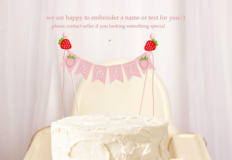 Embroidered name cake topper on pink cotton flags with strawberries on each end. Personalized topper for berry first birthday celebration.