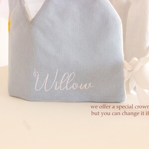 May include: A light blue fabric crown with white embroidery that says "Willow".