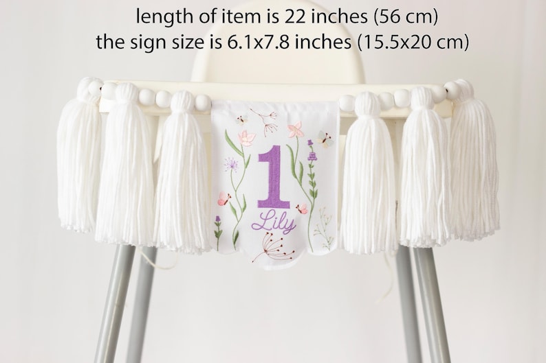Pu&ograve; includere: Striscione bianco per seggiolone con nappe e ricami floreali. Lo striscione &egrave; lungo 56 cm e presenta il numero "1" in viola, il nome "Lily" e un motivo floreale. La dimensione del cartello &egrave; 15,5x20 cm.