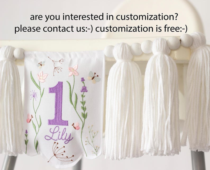 Pu&ograve; includere: Striscione in tessuto bianco con ricami floreali e farfalle, un grande numero 1 viola e il nome "Lily". Lo striscione &egrave; adornato con nappe bianche e perline di legno. Il testo in alto recita "are you interested in customization? please contact us:-) customization is free:-)"