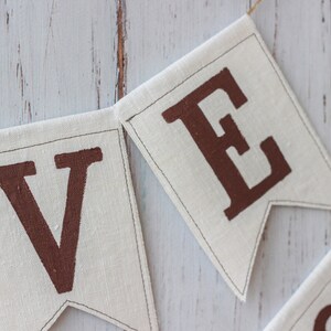 May include: Close-up of a fabric banner with the letters "V" and "E" in brown on a white background. The banner is strung with twine.