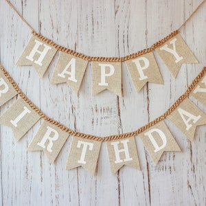 May include: A burlap banner with the words "Happy Birthday" in white letters. The banner is strung with twine and hangs against a whitewashed wood background.