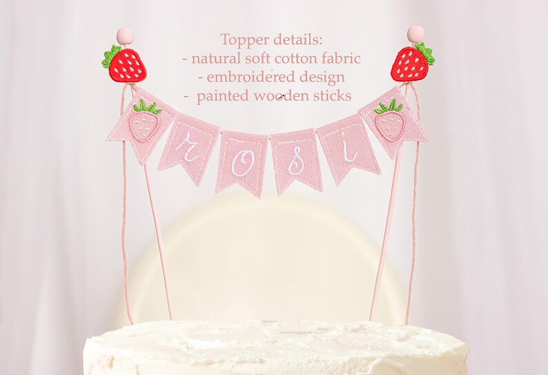 Embroidered name cake topper on pink cotton flags with strawberries on each end. Personalized topper for berry first birthday celebration.