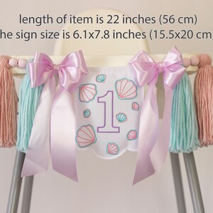 White embroidered mermaid high chair banner with seashells, number one, and lavender bows for a girl’s first birthday.