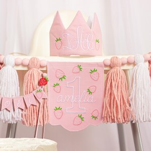 Embroidered name cake topper on pink cotton flags with strawberries on each end. Personalized topper for berry first birthday celebration.