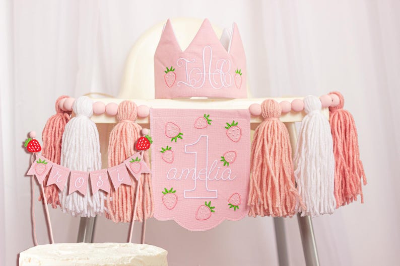 Embroidered name cake topper on pink cotton flags with strawberries on each end. Personalized topper for berry first birthday celebration.
