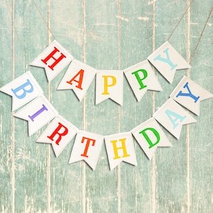 May include: A colorful banner with the words "Happy Birthday" strung on a white wooden background.
