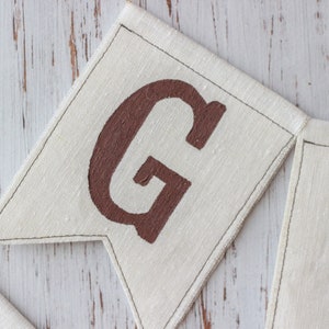 May include: Close-up of a brown fabric banner with the letters "G" and "I" painted in brown. The banner is sewn together with white thread.