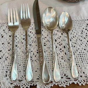 May include: A five-piece silver-toned flatware set consisting of two forks, one dinner knife with a serrated blade, one large spoon, and one smaller spoon. Each piece features a slender handle decorated with an embossed floral pattern.