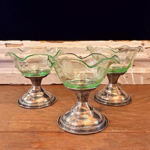 May include: Three small dessert cups featuring light green glass bowls with ruffled edges and etched floral patterns. Each bowl is supported by a polished silver-toned metal pedestal base with a circular foot and a decorative beaded rim detail.