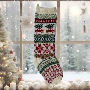 Peut inclure: Une chaussette de Noël tricotée avec un motif festif rouge, vert et blanc. Le motif comprend des rennes, des flocons de neige et des formes géométriques. La chaussette est suspendue devant une fenêtre avec une scène hivernale enneigée.