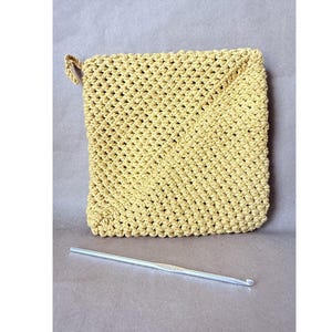 May include: A handmade, square, yellow crochet potholder with a loop for hanging. A silver crochet hook rests below the potholder. The potholder is made with a tight, textured stitch. The background is a solid, neutral color.