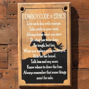 May include: A wooden sign with a black background and white text that reads "Cowboy Code of Ethics". The sign lists a set of rules for living a good life, including "Live each day with courage", "Take pride in your work", "Always finish what you start", "Do what has to be done", "Be tough, but fair", "When you make a promise, keep it", "Ride for the brand", "Talk less and say more", "Know where to draw the line", "Always remember that some things aren't for sale".