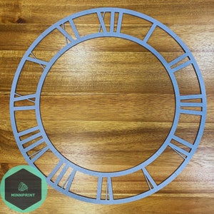 May include: A silver-coloured, open-faced clock frame with Roman numerals. The circular frame is made of metal and sits on a wooden surface. The clock face has the logo "MINNPRINT" in the lower left corner.