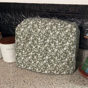 以下が含まれることがあります： 緑色の花柄の家電カバー、木製の蓋が付いた「FLOUR」と「SUGAR」と書かれた2つの白いキャニスター、ストライプのマグカップが付いた木製のマグツリーを備えたキッチンシーン。