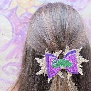 May include: Purple and gold glitter hair bow with a green chameleon design.
