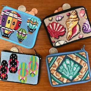 May include: Four small zippered pouches with different embroidered designs. The pouches are blue, beige, and light blue. The designs include hot air balloons, seashells, flip flops, and a seashell in a geometric pattern.
