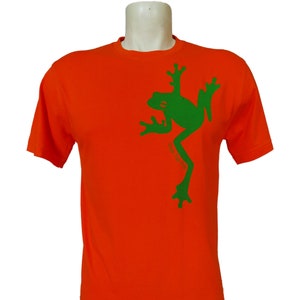 May include: Orange t-shirt featuring a green frog graphic. The frog is facing right with its arms raised above its head. The text "Green for Earth" is printed below the frog.