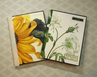 May include: Two rectangular journals with black edges. The left journal features a large yellow sunflower and the text AUTUMN SUNFLOWER. The right journal displays white roses with green stems and the text ROSE, ORDER No. 3568, REQ No. 1620.