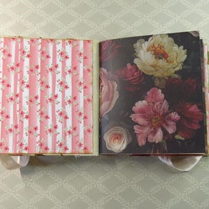 May include: An open scrapbook with two distinct pages. The left page features a vertical pink and white striped pattern with small red floral accents. The right page displays a dark background with a large, detailed illustration of blooming flowers.