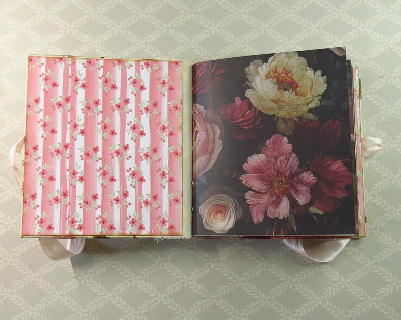 May include: An open scrapbook with two distinct pages. The left page features a vertical pink and white striped pattern with small red floral accents. The right page displays a dark background with a large, detailed illustration of blooming flowers.
