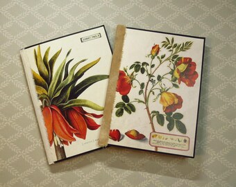 May include: Two rectangular journals with botanical illustrations. The left journal features a red crown imperial flower and the text 22817.762.3. The right journal displays a rose plant with red and yellow blossoms and a small text box at the bottom.