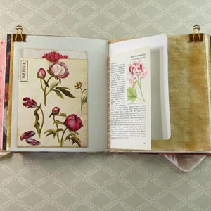 May include: An open scrapbook with two pages featuring vintage-style botanical illustrations of pink peonies and a printed page about Pelargonium plants. The pages are held open by gold metal binder clips and include a vertical pocket with the word OVERDUE.