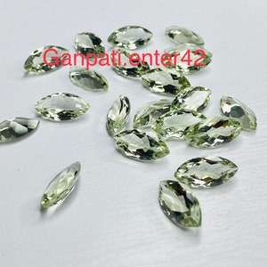 May include: A collection of light green marquise cut gemstones. The gemstones are scattered on a white surface.