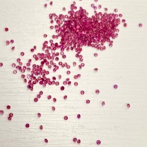 Può includere: Una dispersione di piccole pietre preziose di rubino rotonde e rosa, di circa 1,2 mm di diametro. Il testo "Ruby round 1.2x1.2 MM" è visibile nella parte inferiore dell'immagine.
